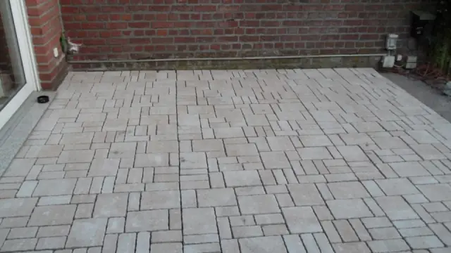 Helle Natursteinpflasterfläche vor einer Backsteinwand