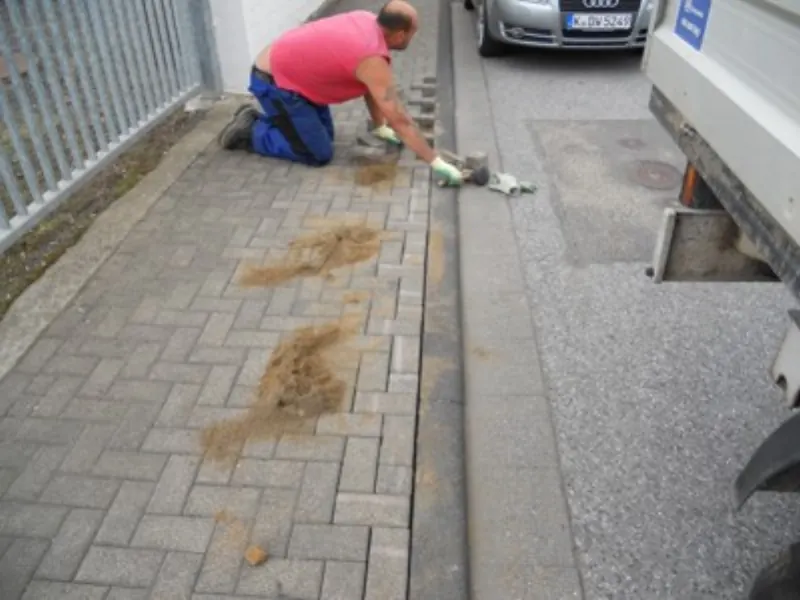 Mitarbeiter kniet beim Setzen von Pflastersteinen am Rand einer Fläche