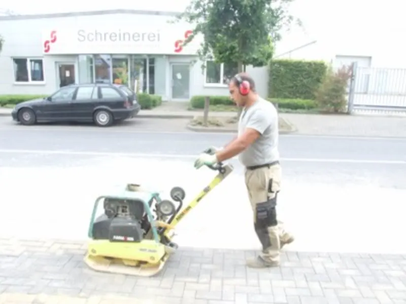 Mitarbeiter verdichtet eine neu gepflasterte Fläche mit einer Rüttelplatte